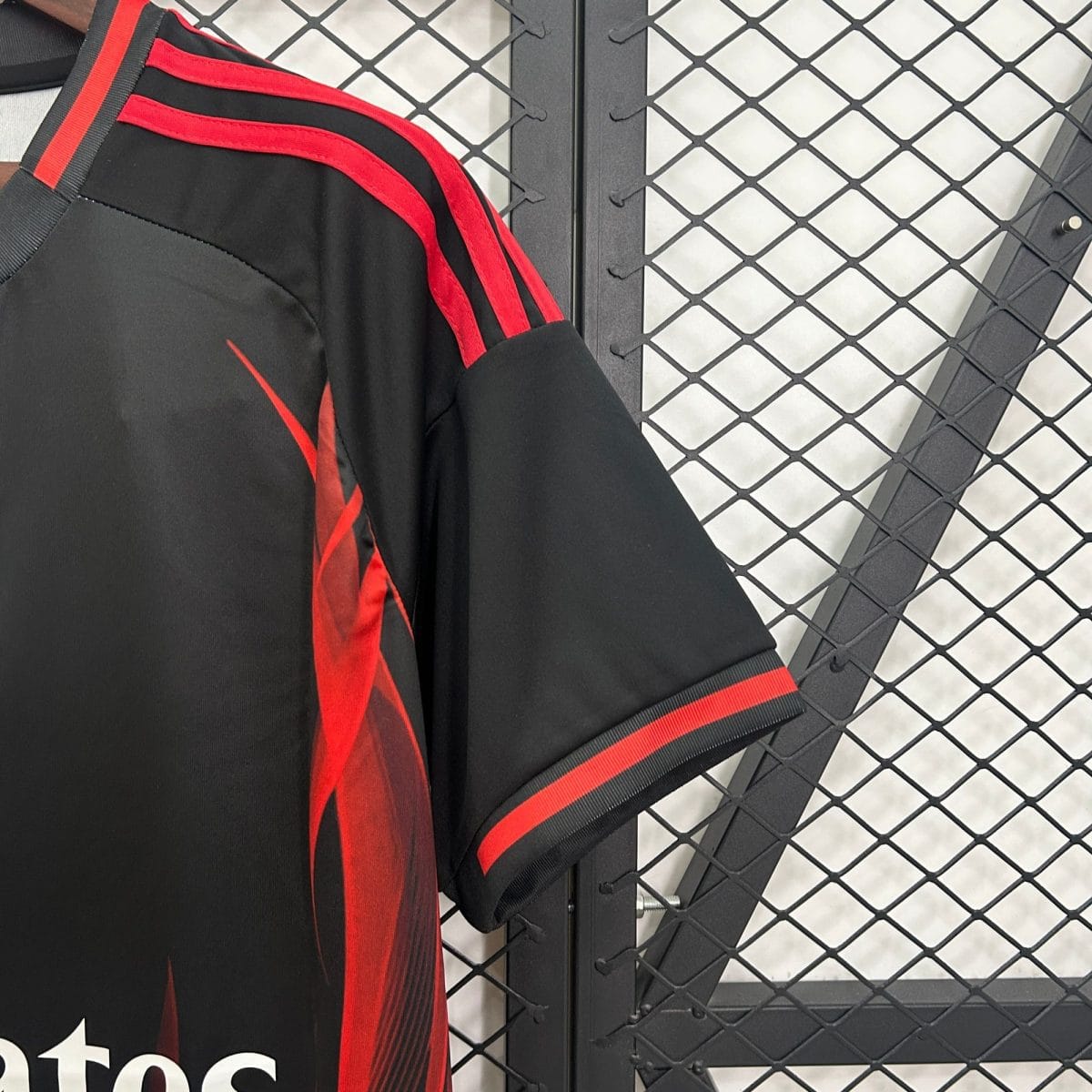 Black jacket with red stripes hanging on a black metal diamond-pattern fence.