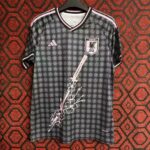 Black Japan national football team jersey with pink trim on a hanger; features a repeating circular pattern, pink Adidas logo, and a JFA crest on the chest with a white and pink sword-and-floral graphic cascading down the front.