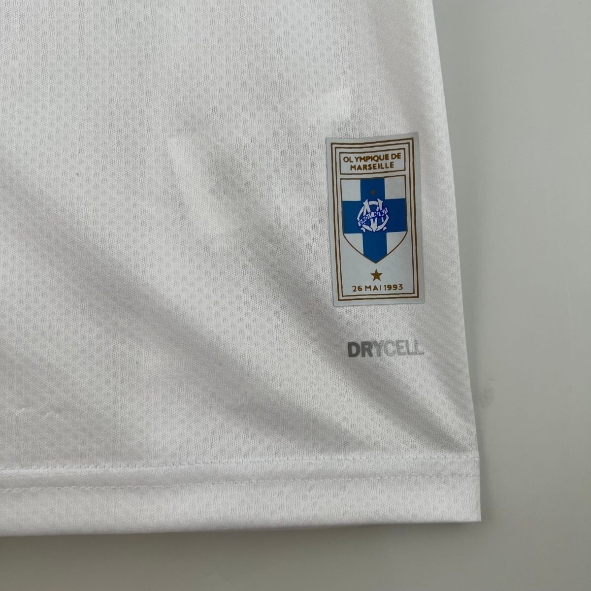 Close-up of white fabric with a small Olympique de Marseille badge sewn onto the sleeve.