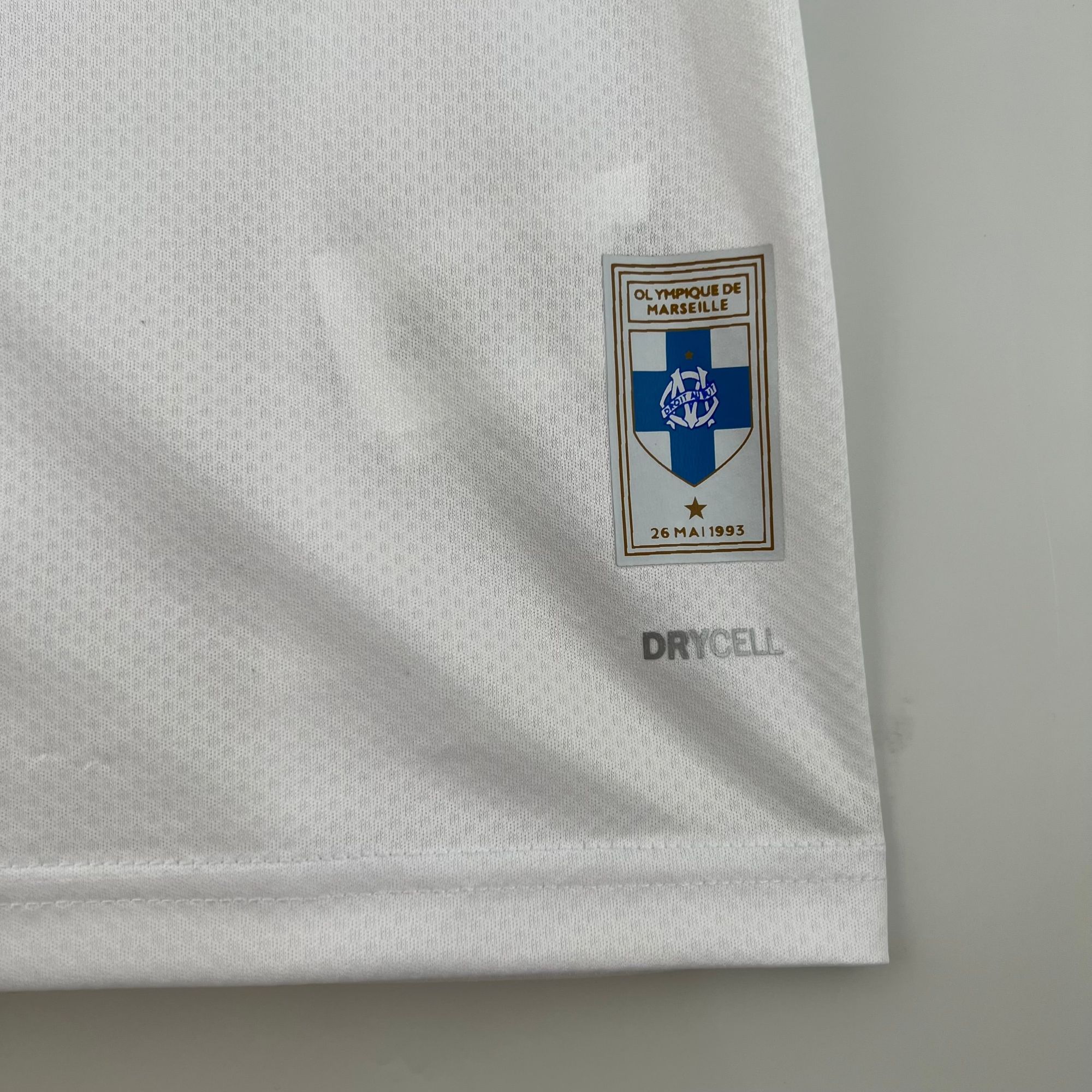 e733f73b_5c4a61ef-92fe-4383-8b48-734272b085d7 | UAE SPORT STORE Close-up of white fabric with a small Olympique de Marseille badge sewn onto the sleeve.