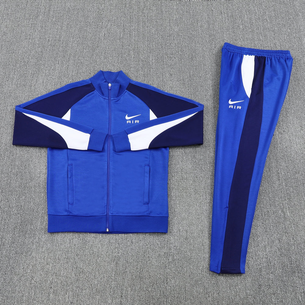e777fcf6 | UAE SPORT STORE Blue Nike Air tracksuit jacket and matching pants laid flat on a gray surface, with white and dark blue panel accents.
