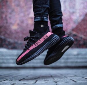 Close-up of black sneakers with a pink stripe reading 'SPLY-350' in mid-air as the wearer jumps.
