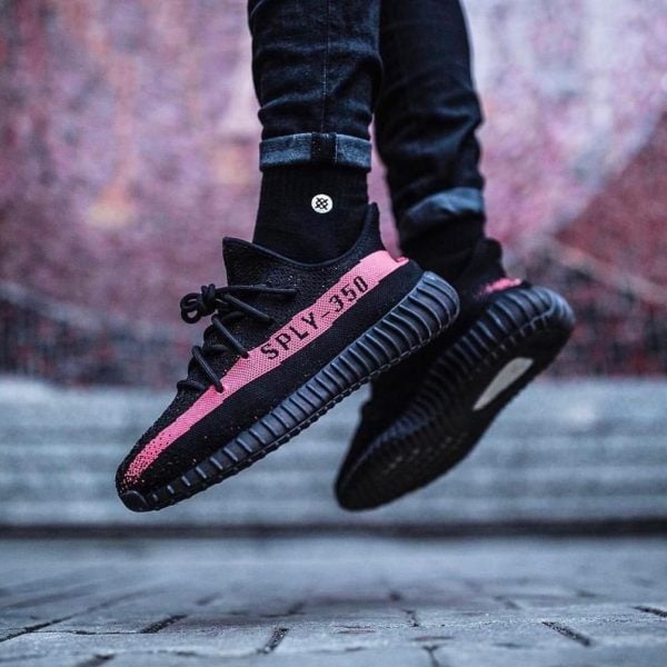 Close-up of black sneakers with a pink stripe reading 'SPLY-350' in mid-air as the wearer jumps.