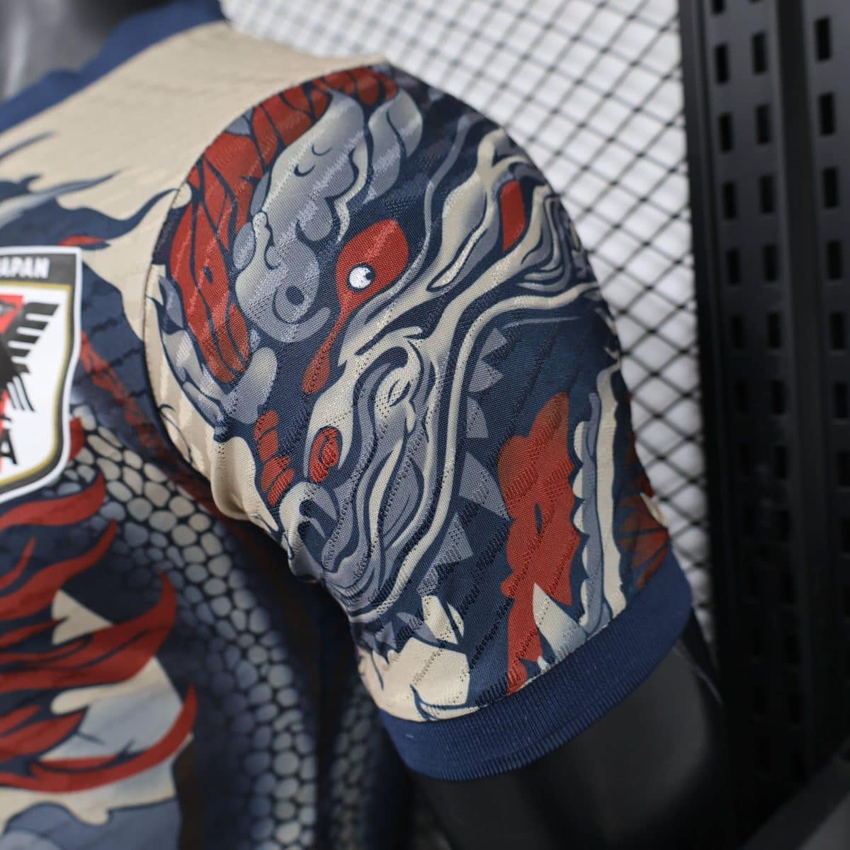 Close-up of patterned fabric with red, blue, and beige swirls and visible stitching, likely part of a garment or gear.