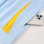 Close-up of light blue fabric with a yellow stripe and part of a silver smartphone in the lower right corner.