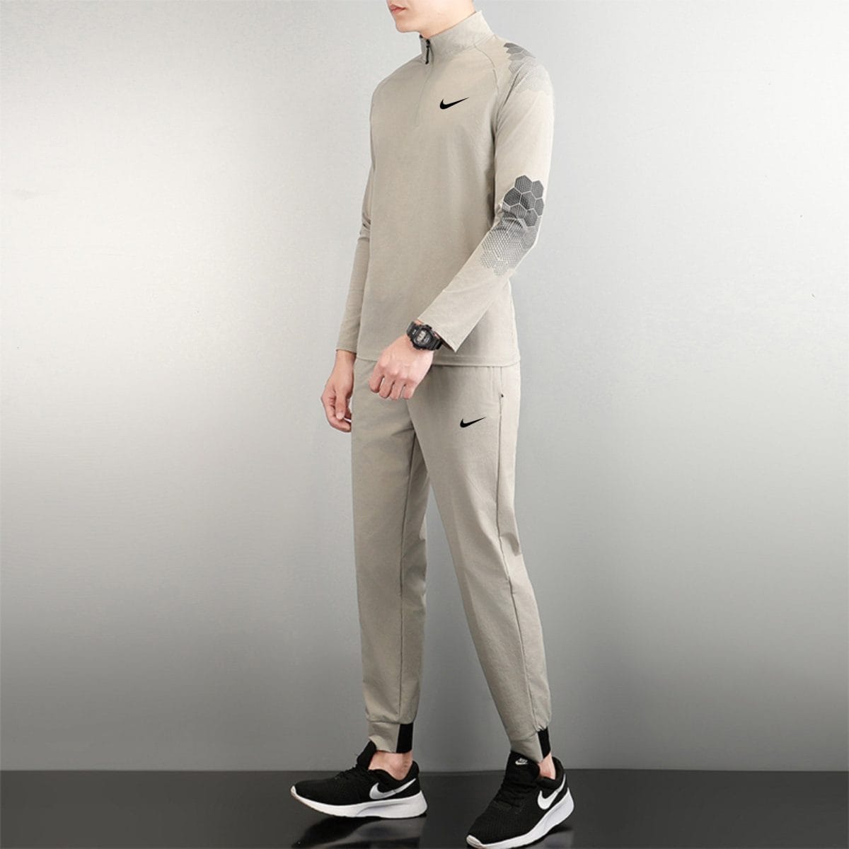 Side view of a person wearing a light gray Nike athletic top and pants, with black Nike shoes, standing against a neutral background.