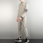 Side view of a person wearing a light gray Nike athletic top and pants, with black Nike shoes, standing against a neutral background.