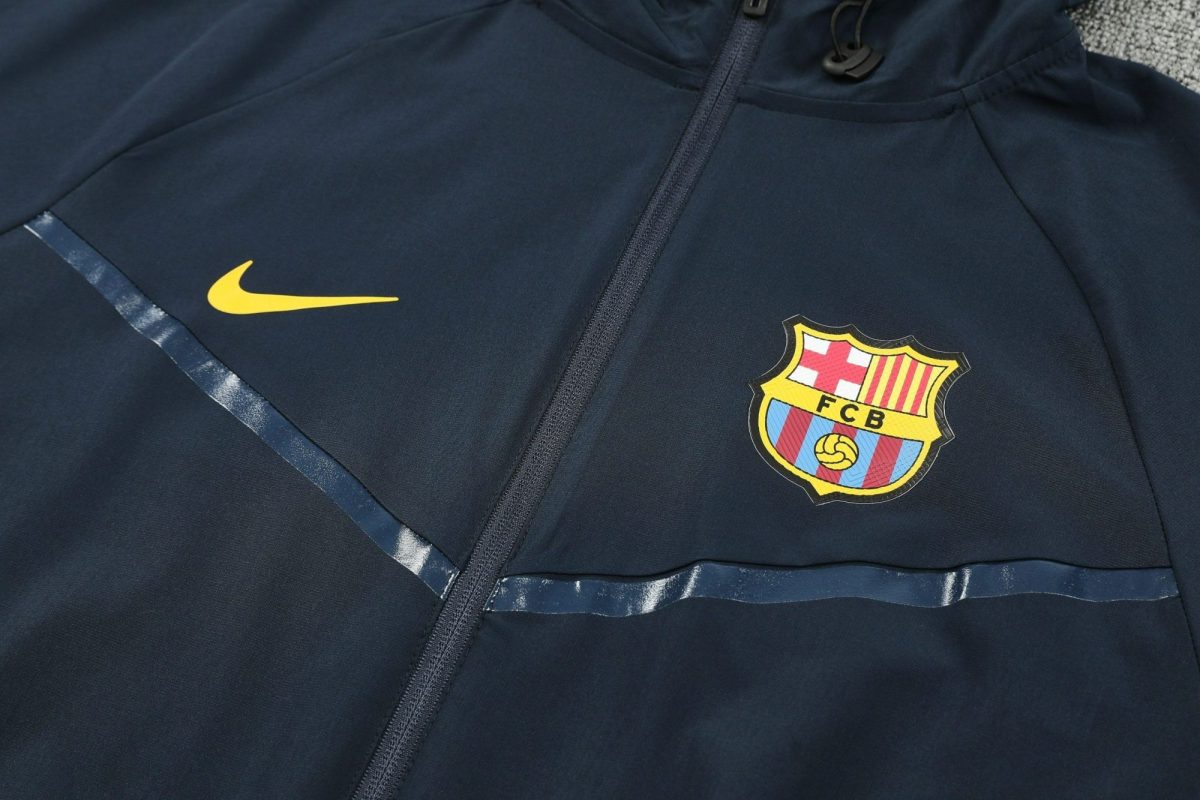 Navy sports jacket featuring a yellow Nike swoosh and FC Barcelona crest near a central zipper.
