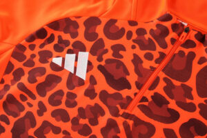 Orange jacket with black leopard print fabric, featuring a bright orange zipper and a white three-stripe emblem near the chest area.