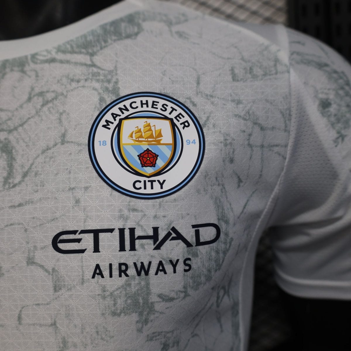 Close-up of a Manchester City badge on light gray patterned fabric.