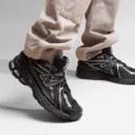 Close-up of black New Balance running shoes with silver accents on a person wearing beige pants.