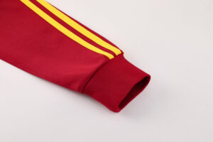 Red track jacket sleeve with two yellow stripes and a ribbed cuff on a light background.