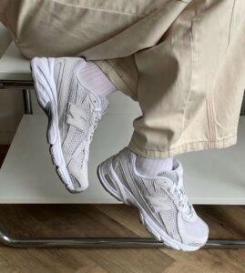 White New Balance sneakers on a person wearing beige pants, legs crossed while sitting on a chair, close-up shot.