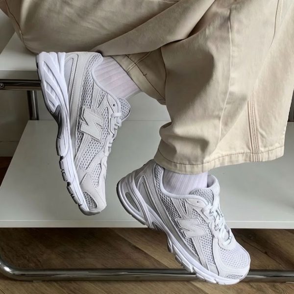 White New Balance sneakers on a person wearing beige pants, legs crossed while sitting on a chair, close-up shot.