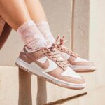 Rose-pink and white sneakers with pink laces, worn with pink patterned socks, perched on a stone ledge.