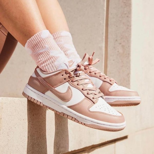Rose-pink and white sneakers with pink laces, worn with pink patterned socks, perched on a stone ledge.