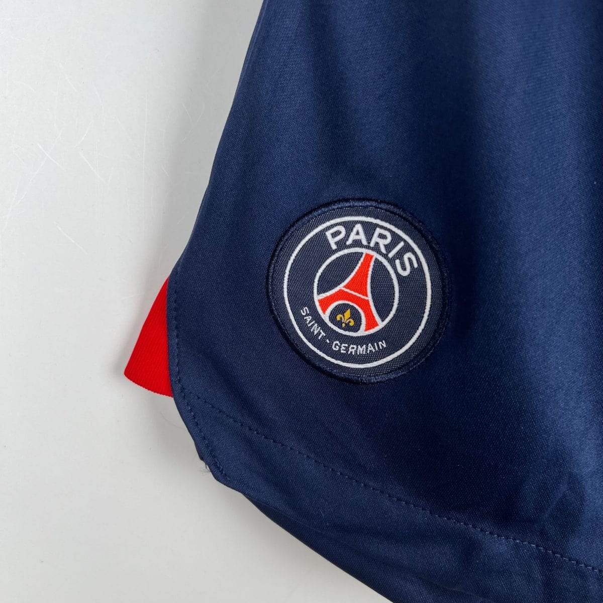 Close-up of navy fabric with a round Paris Saint-Germain patch and a red stripe.