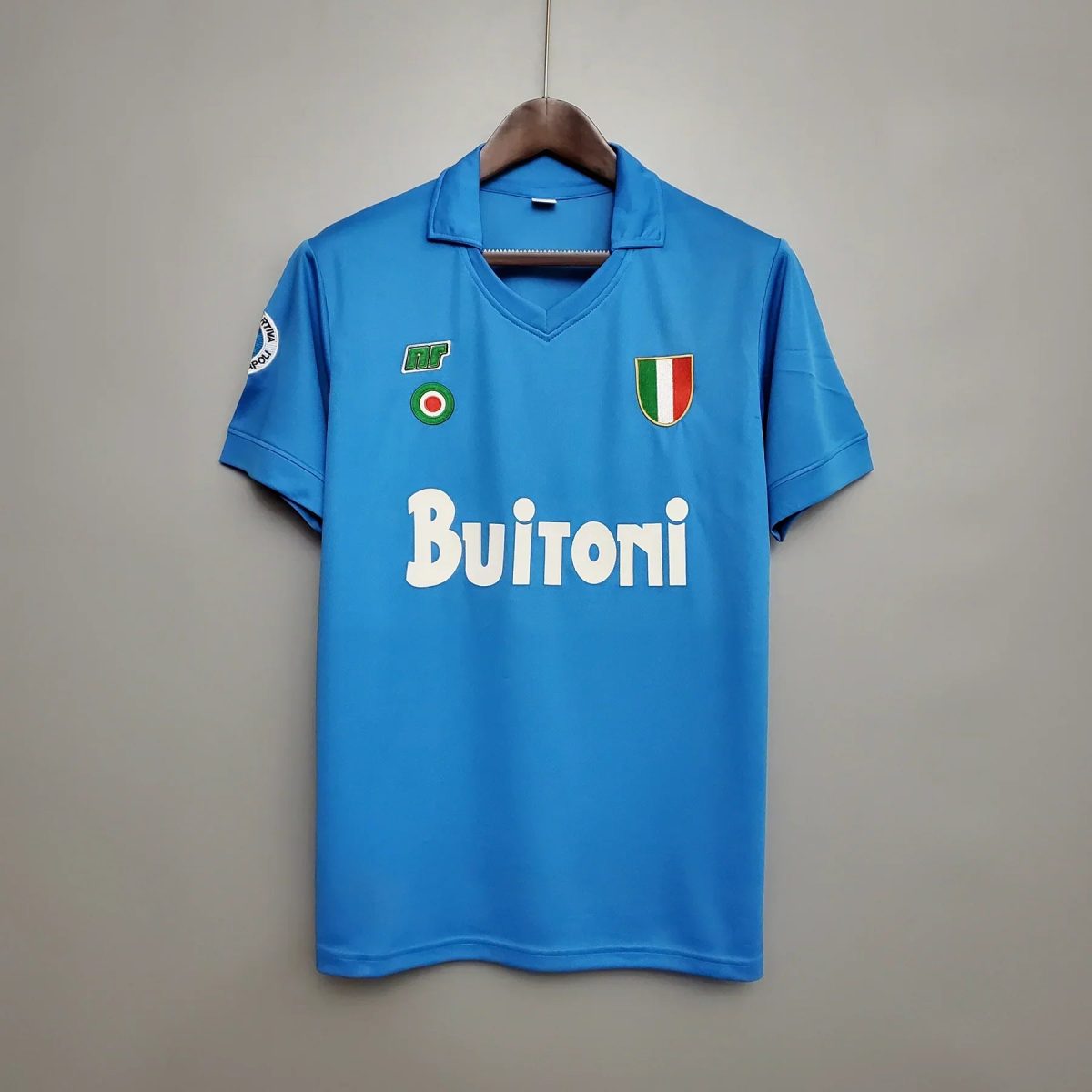 Bright blue polo shirt on a wooden hanger, featuring an Italian flag crest on the left chest and multiple sponsor patches on the front.