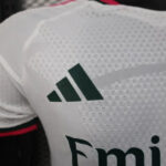 Close-up of a white sports jersey showing a green Adidas logo and part of the Emirates branding.