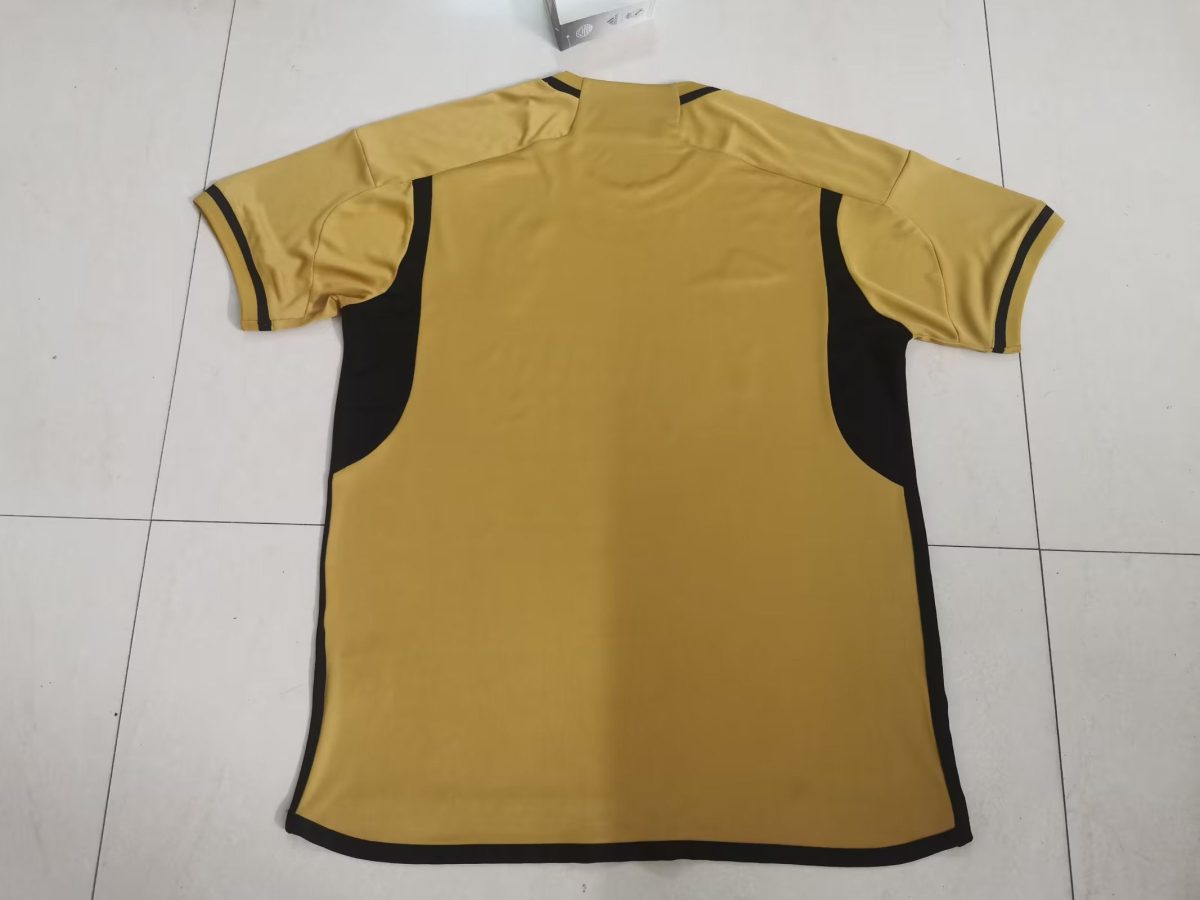 Back view of a yellow short-sleeve polo shirt with black side panels and black sleeve cuffs laid on a white tiled floor