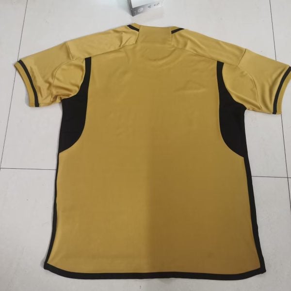 Back view of a yellow short-sleeve polo shirt with black side panels and black sleeve cuffs laid on a white tiled floor