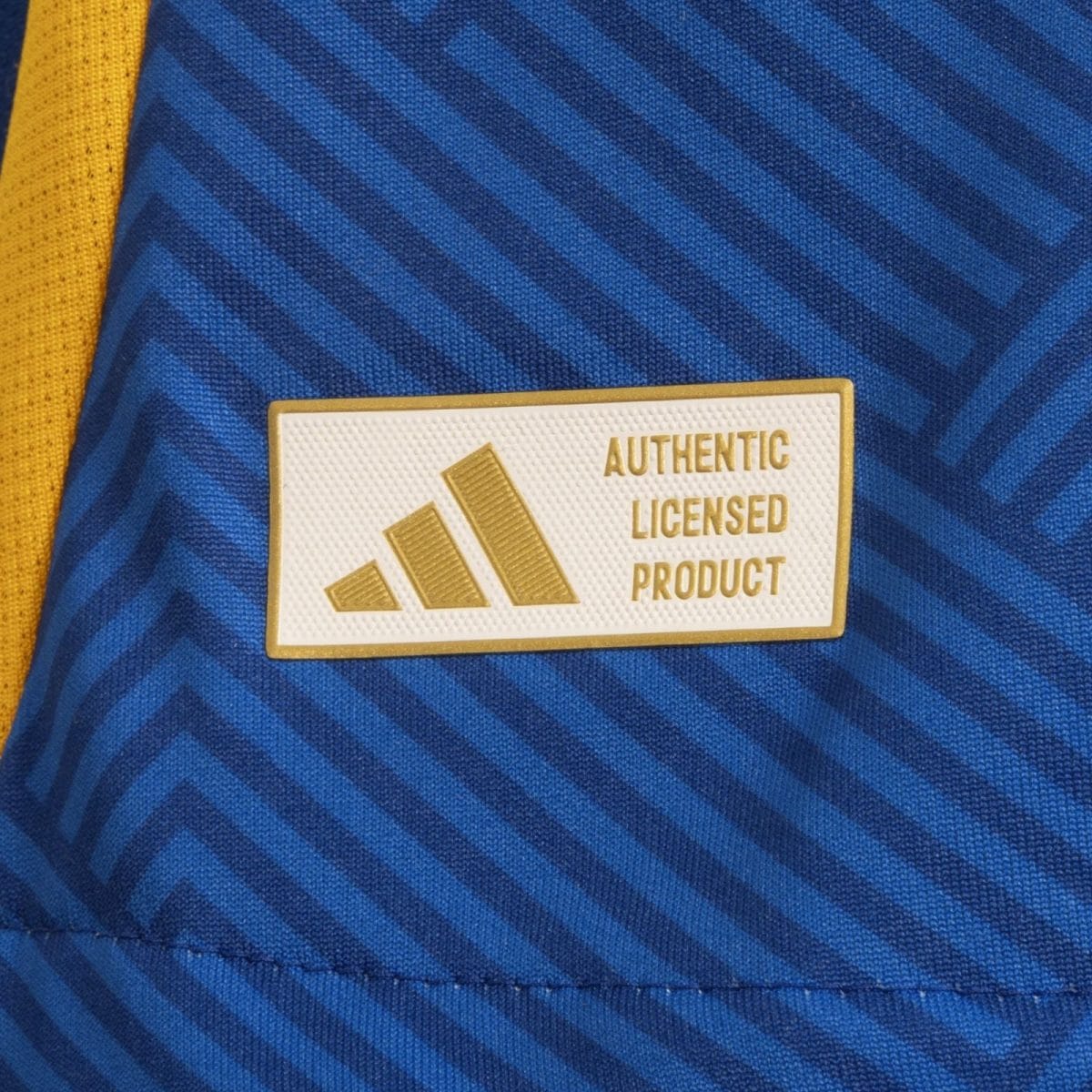 Close-up of blue striped fabric with a yellow strap and a white patch reading 'AUTHENTIC LICENSED PRODUCT' in gold with a three-bar logo, indicating licensed merchandise.