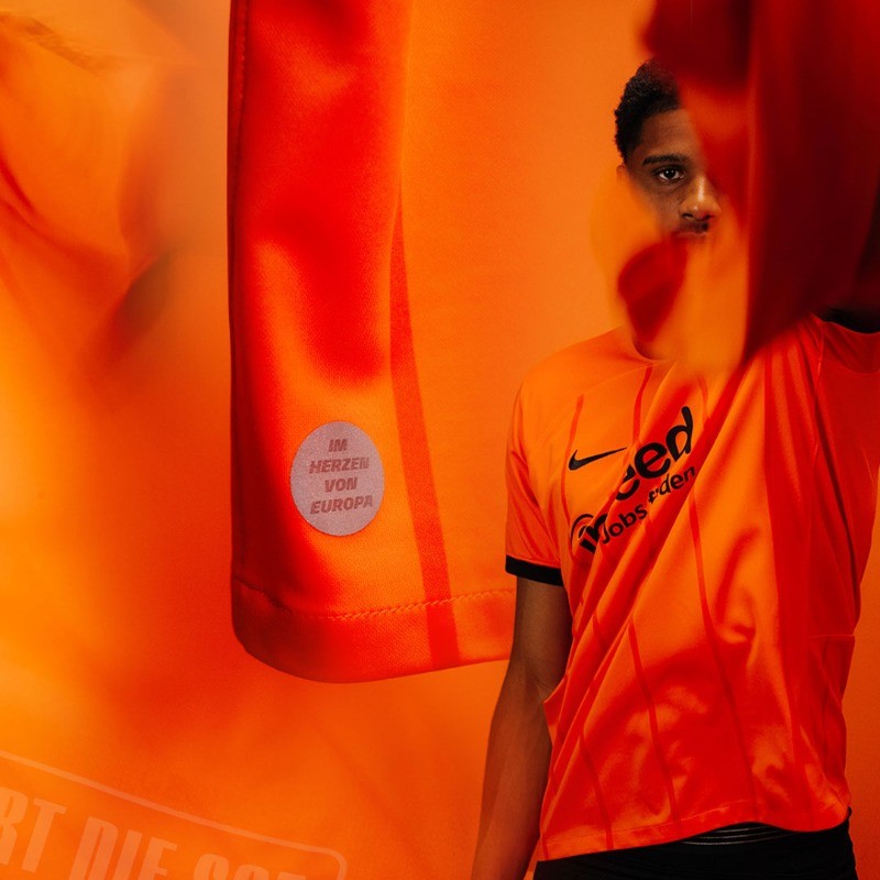 eWGGMFwA4kjuOdU | UAE SPORT STORE Person in an orange sports jersey standing against an orange backdrop, with a circular sticker reading 'IM HERZEN VON EUROPA' on the fabric.