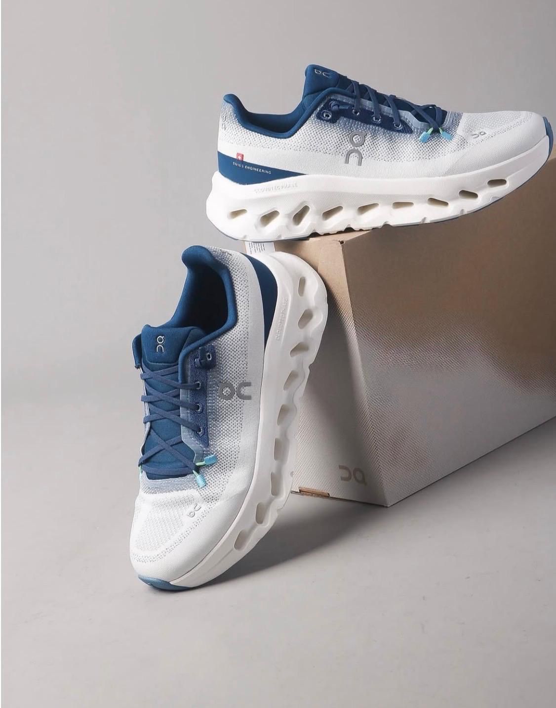 ea282003-4e62-4fd0-80d0-0366dbe9ddc2 | UAE SPORT STORE White and blue On running shoes with a thick white outsole resting on a cardboard box.