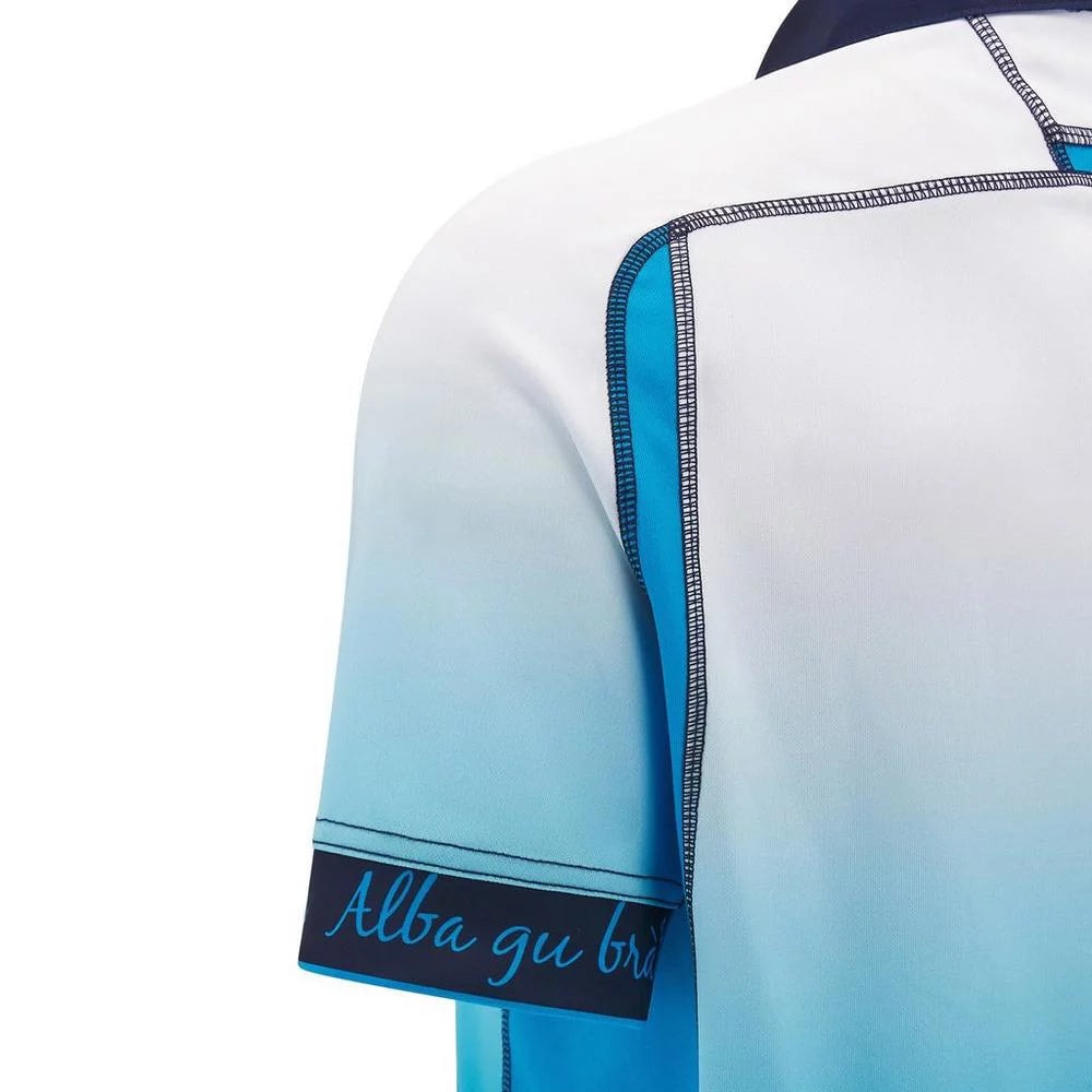 eae260dcf1429049d0d039a9f244c119 | UAE SPORT STORE Close-up of a blue gradient polo shirt sleeve with visible stitching and a dark hem label that reads 'Alba gu br'.