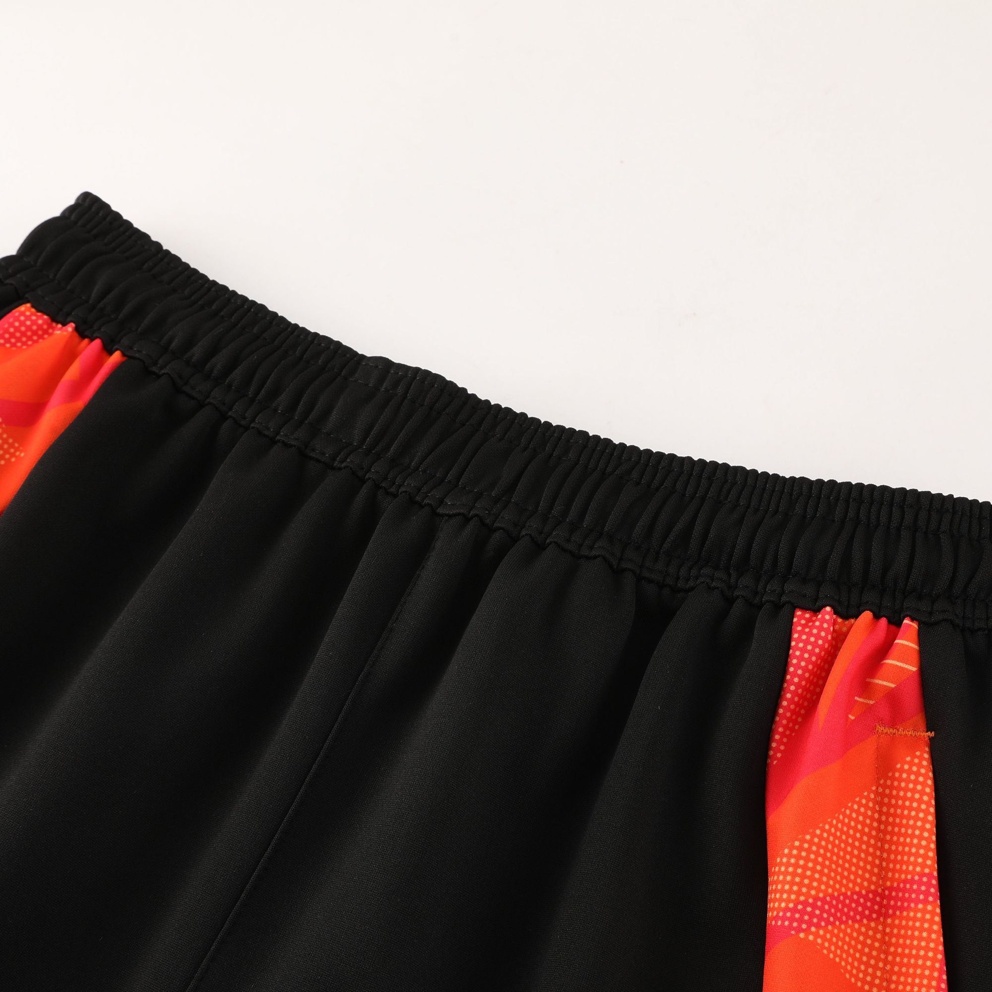 eb828396 | UAE SPORT STORE Close-up of black fabric with an elastic waistband, with a red patterned stripe along the side edge.