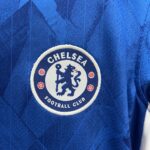Close-up of blue fabric with a circular white-and-blue Chelsea Football Club embroidered patch (partial view).