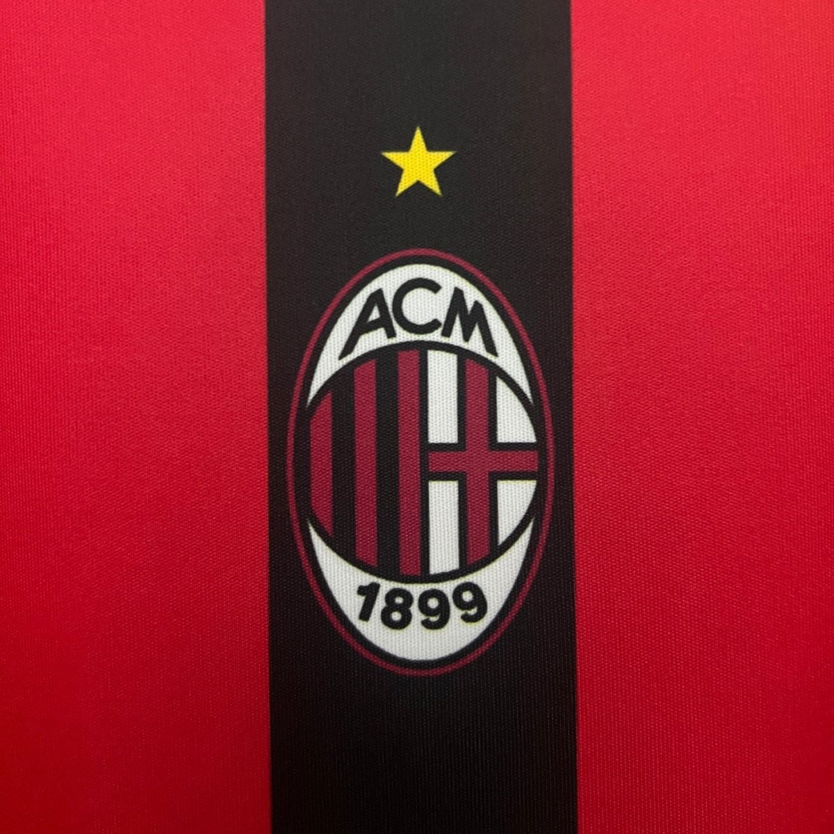 Close-up of a red jersey with a black vertical band and AC Milan crest, including a yellow star above the badge and year 1899 at the bottom text.