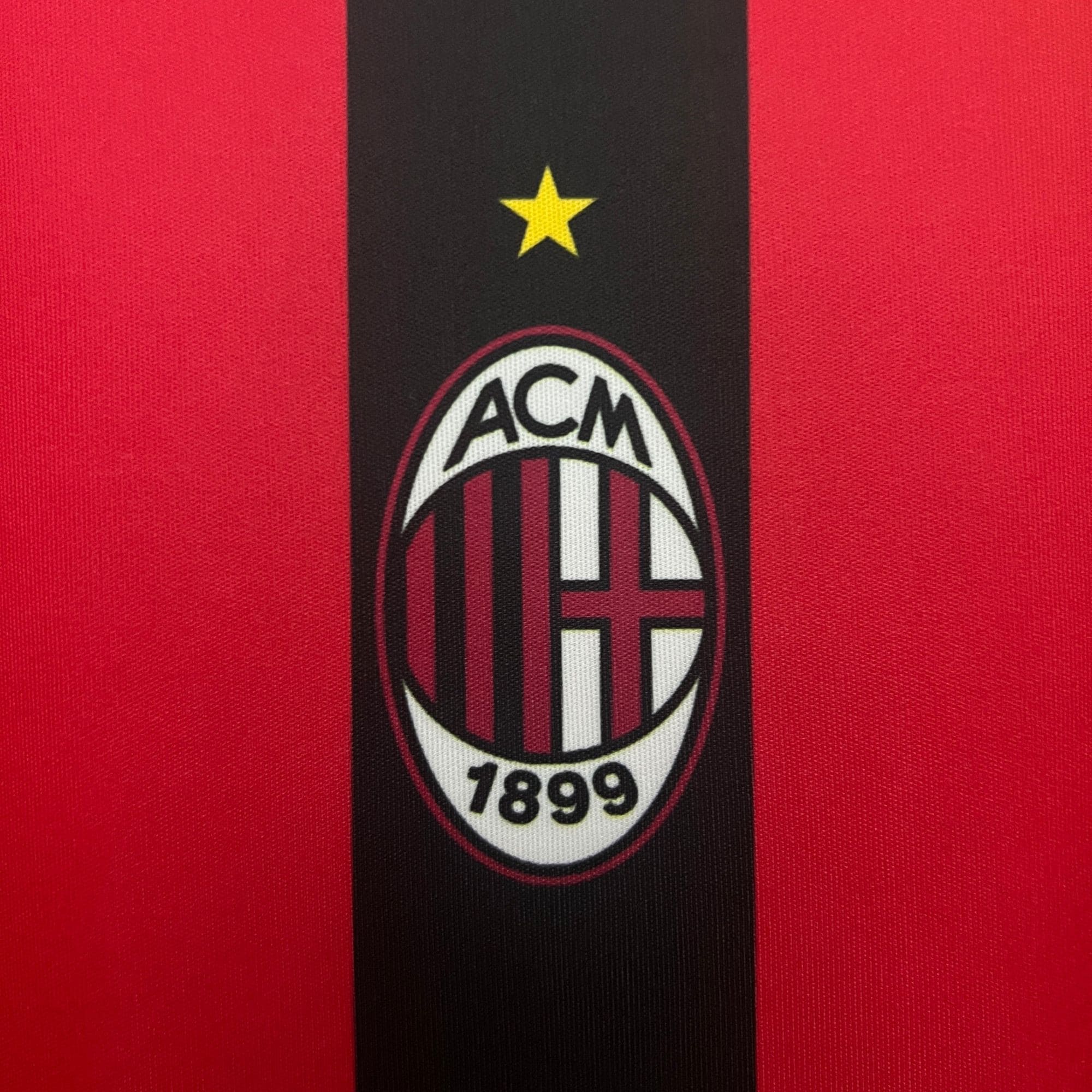 ec58db37 | UAE SPORT STORE Close-up of a red jersey with a black vertical band and AC Milan crest, including a yellow star above the badge and year 1899 at the bottom text.
