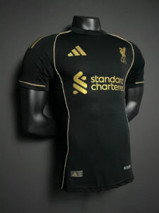 Black Liverpool FC football jersey on a mannequin with gold sponsor and trim, Adidas logo, and club crest visible on the chest