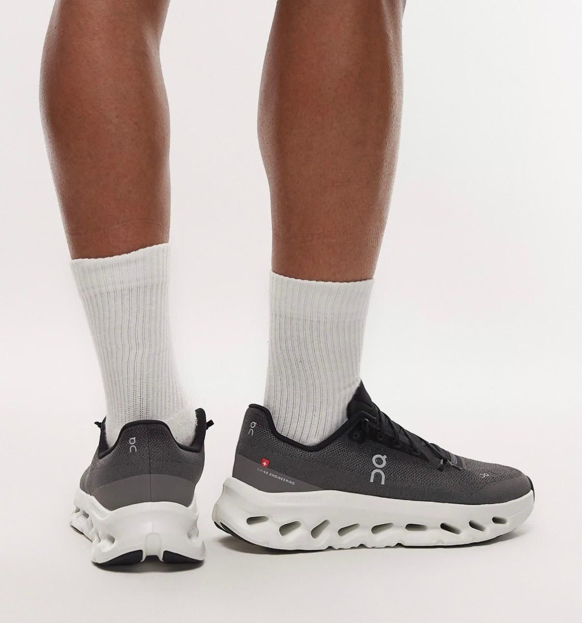 Athletic gray running shoes with a chunky white sole, worn with white crew socks, viewed from the back on a white background.