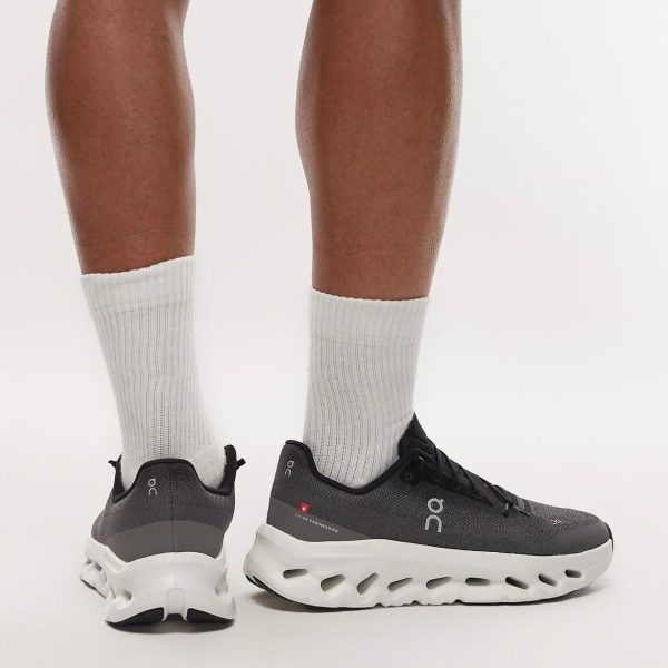 Athletic gray running shoes with a chunky white sole, worn with white crew socks, viewed from the back on a white background.