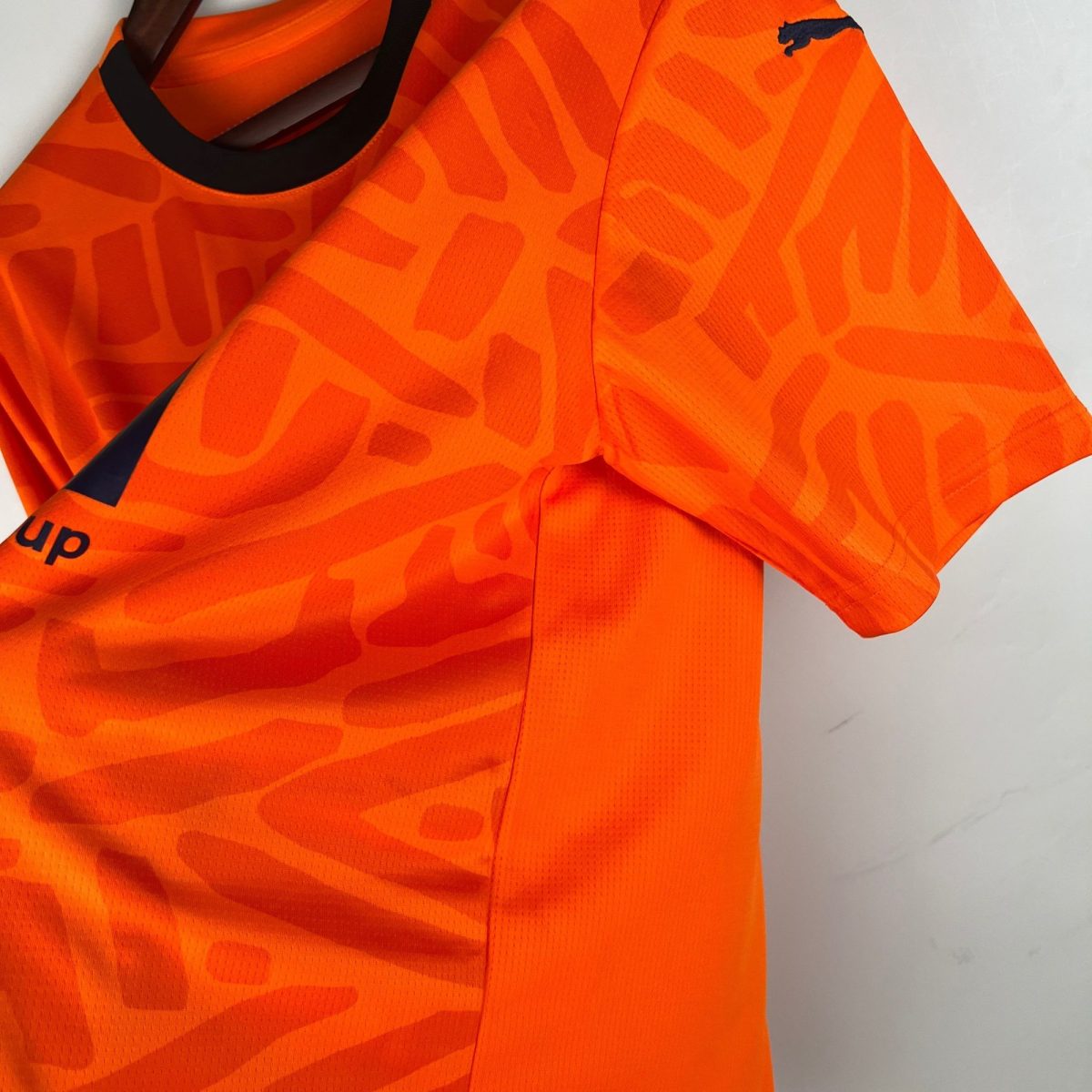 Close-up of a bright orange high-visibility jacket with a black Puma logo on the shoulder.