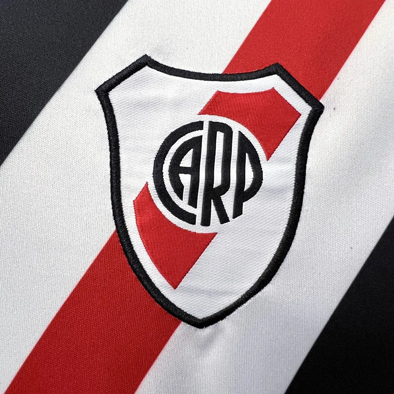 ecf053b08ccb2ef7_fde50ea3-8327-4369-94dd-652e0133222e | UAE SPORT STORE Close-up of a shield badge with a circular monogram on a white jersey featuring a red diagonal stripe and black border.