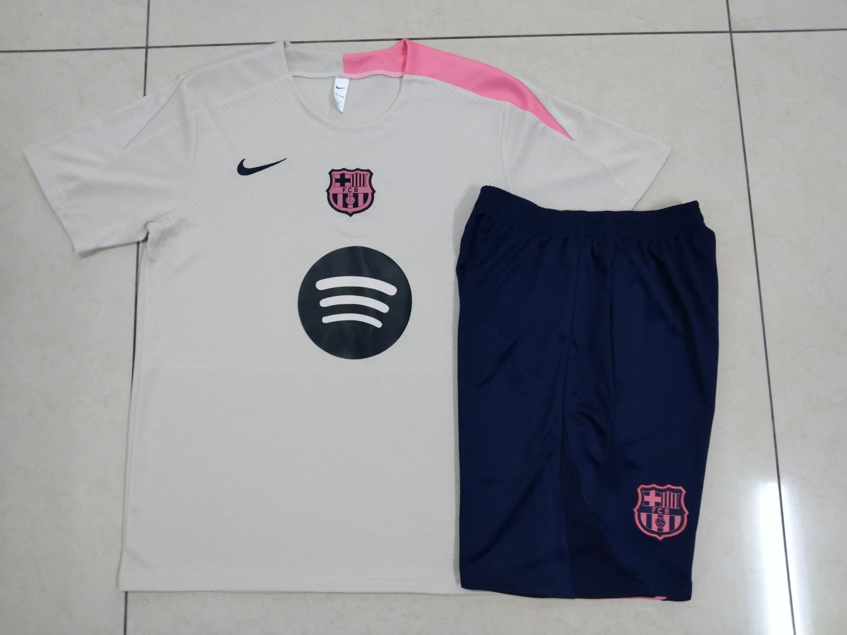 ed1cf881 | UAE SPORT STORE White FC Barcelona soccer jersey with pink shoulder accent, navy Nike swoosh, pink crest, and Spotify logo on the chest, paired with navy shorts on a tiled floor