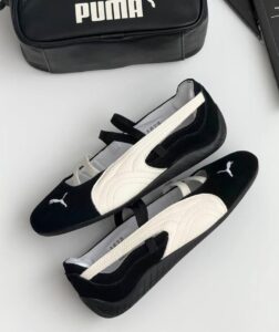 ed456981-ffca-4072-8d08-79a98f337978 | UAE SPORT STORE Two-tone Puma slip-on sneakers (black with white accents) placed on a light surface beside a black Puma bag, visible logo on the toe.