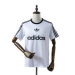 White Adidas T-shirt on a mannequin with black trefoil logo and three black stripes along sleeves.