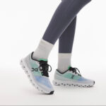 Person wearing pastel gradient On running shoes (blue to mint) with white cushioned sole, gray leggings, and white crew socks on a white background.