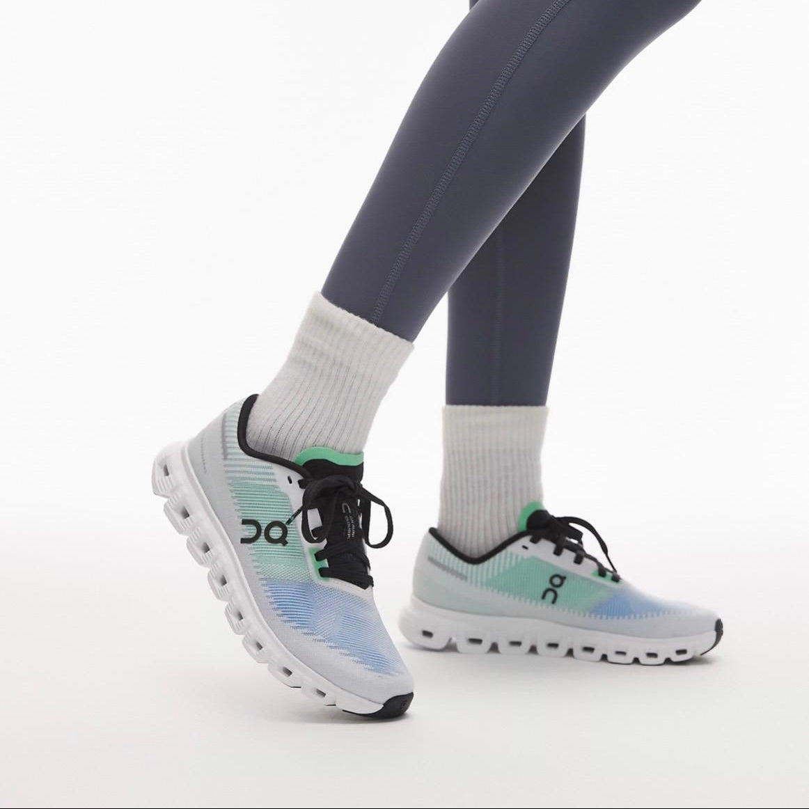 eda32585-b74f-4f70-aa28-e756f20e4040 Person wearing pastel gradient On running shoes (blue to mint) with white cushioned sole, gray leggings, and white crew socks on a white background.