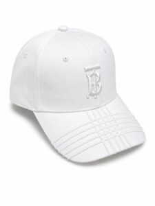 White baseball cap with a stitched monogram on the front, curved brim with decorative stitching, and small ventilation eyelets.