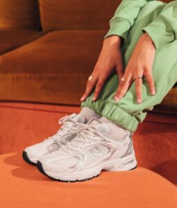 Person wearing white running sneakers and light green sweatpants, resting hands on knees while seated on an orange surface.