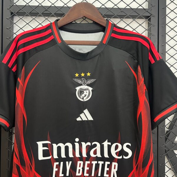 Black football jersey on hanger with red stripes, crest, three gold stars, and 'Emirates Fly Better' slogan visible