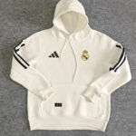 White Real Madrid hoodie with hood, Adidas logo on chest and Real Madrid crest, and black stripe accents on the sleeves (front pocket visible).