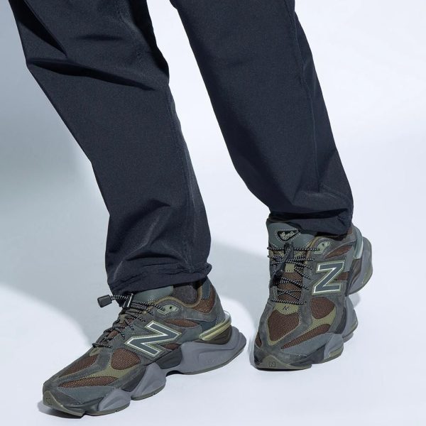 Person wearing dark pants and gray-green hiking sneakers with a prominent 'N' logo.