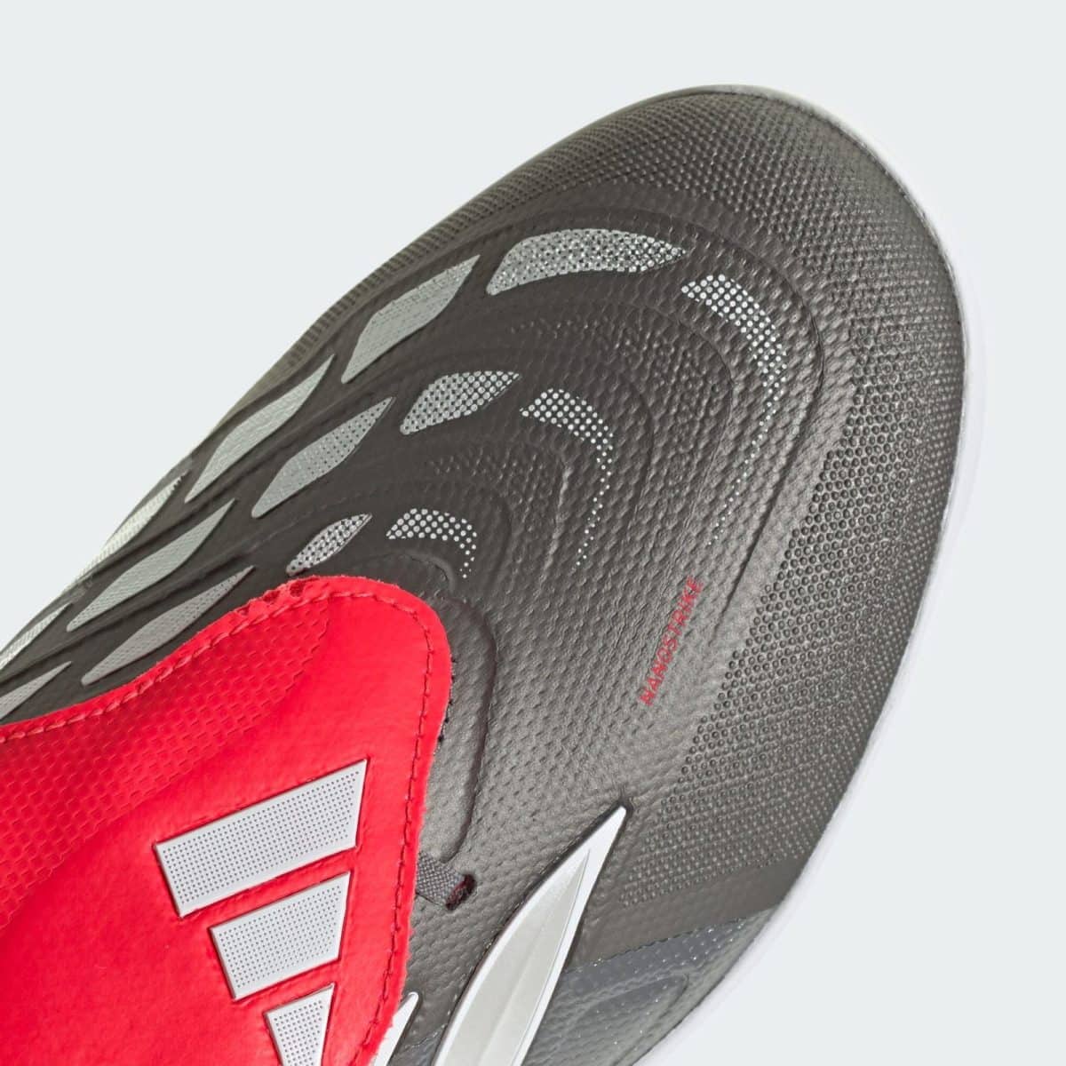 Close-up of a black athletic shoe with a red tongue, textured upper, and gray reflective accents.