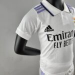 Close-up of a white sports polo with purple shoulder stripes and Adidas logo on the chest area, on a black mannequin.